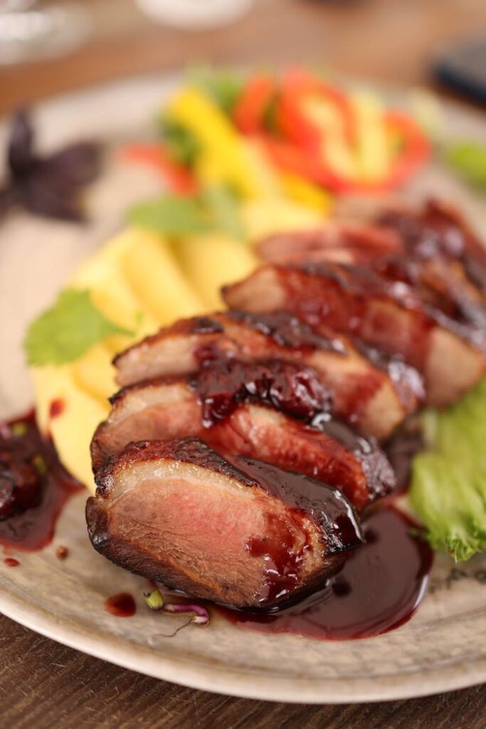 Sliced duck breast served with a rich sauce and fresh fruit garnish, showcasing gourmet dining.