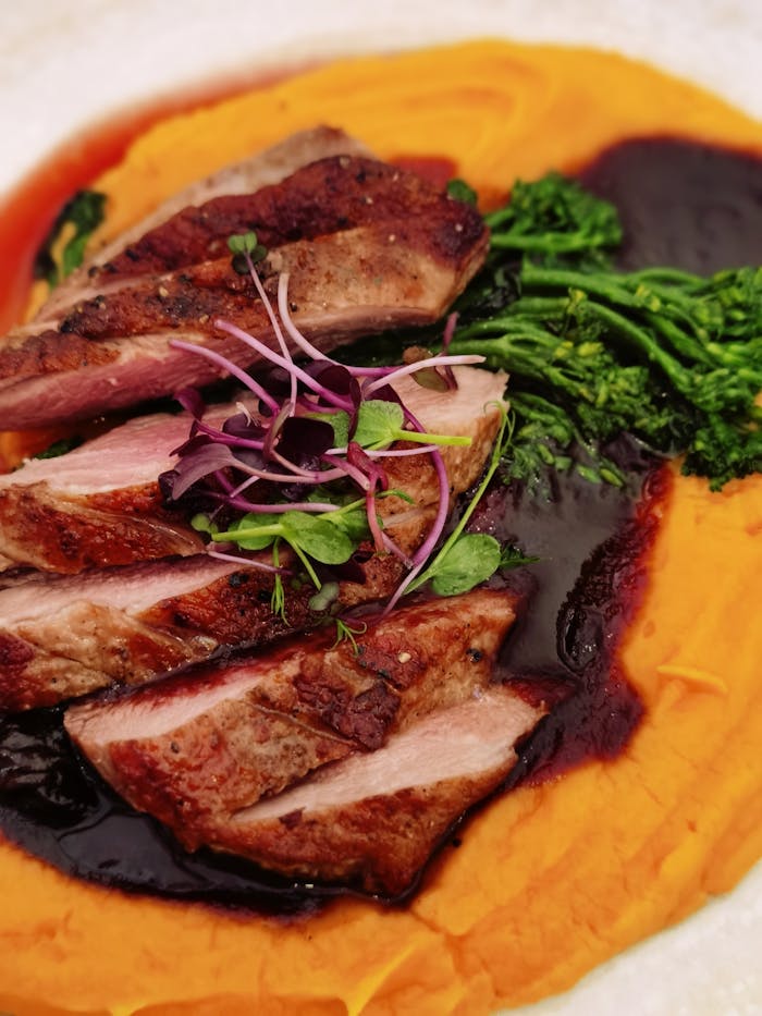 Sliced duck breast with vibrant mashed sweet potatoes and broccolini, garnished for a gourmet touch.